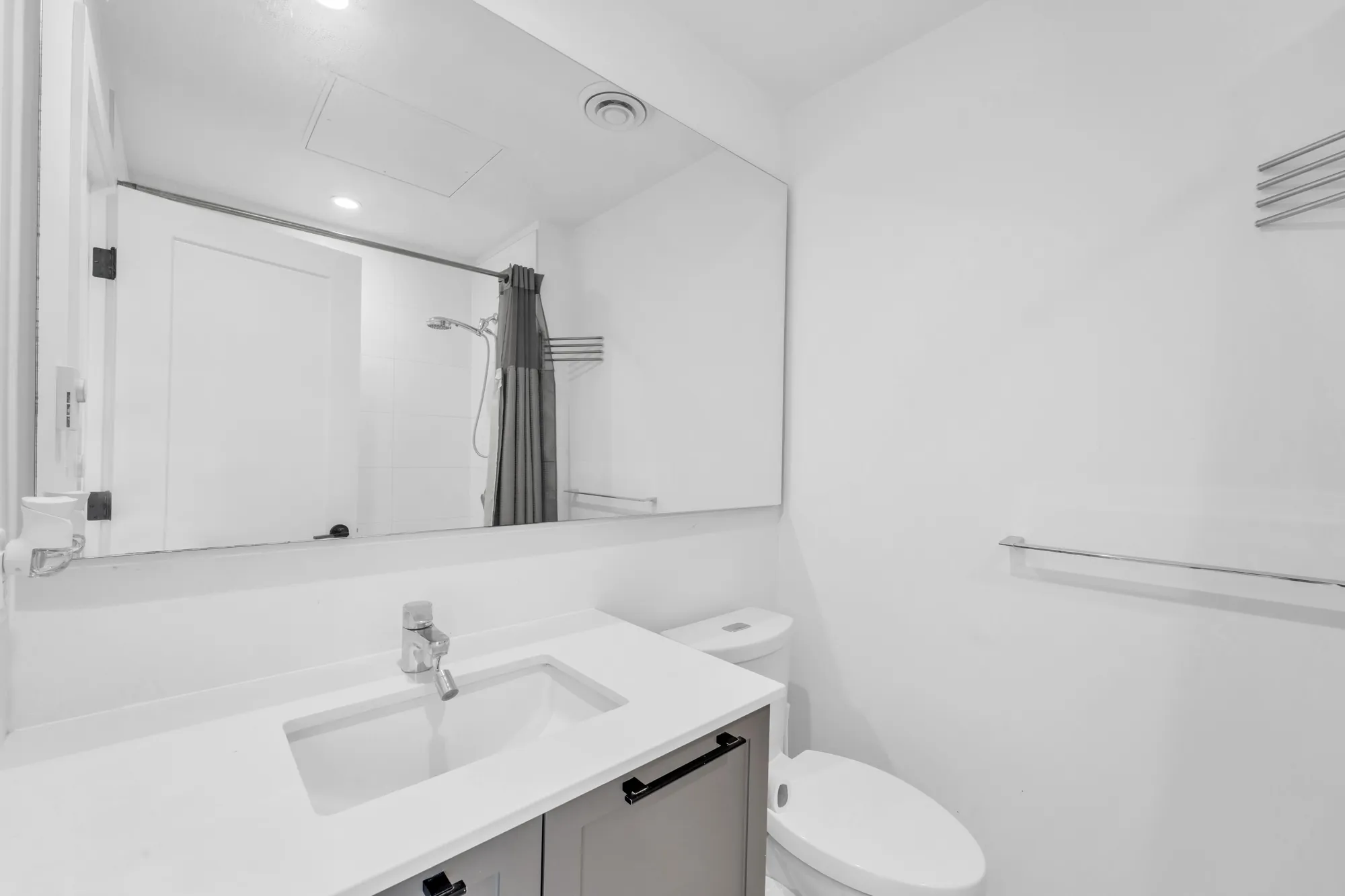 The main bathroom: a white vanity with a wide mirror, a toilet, the tub and its shower curtain reflected in the mirror