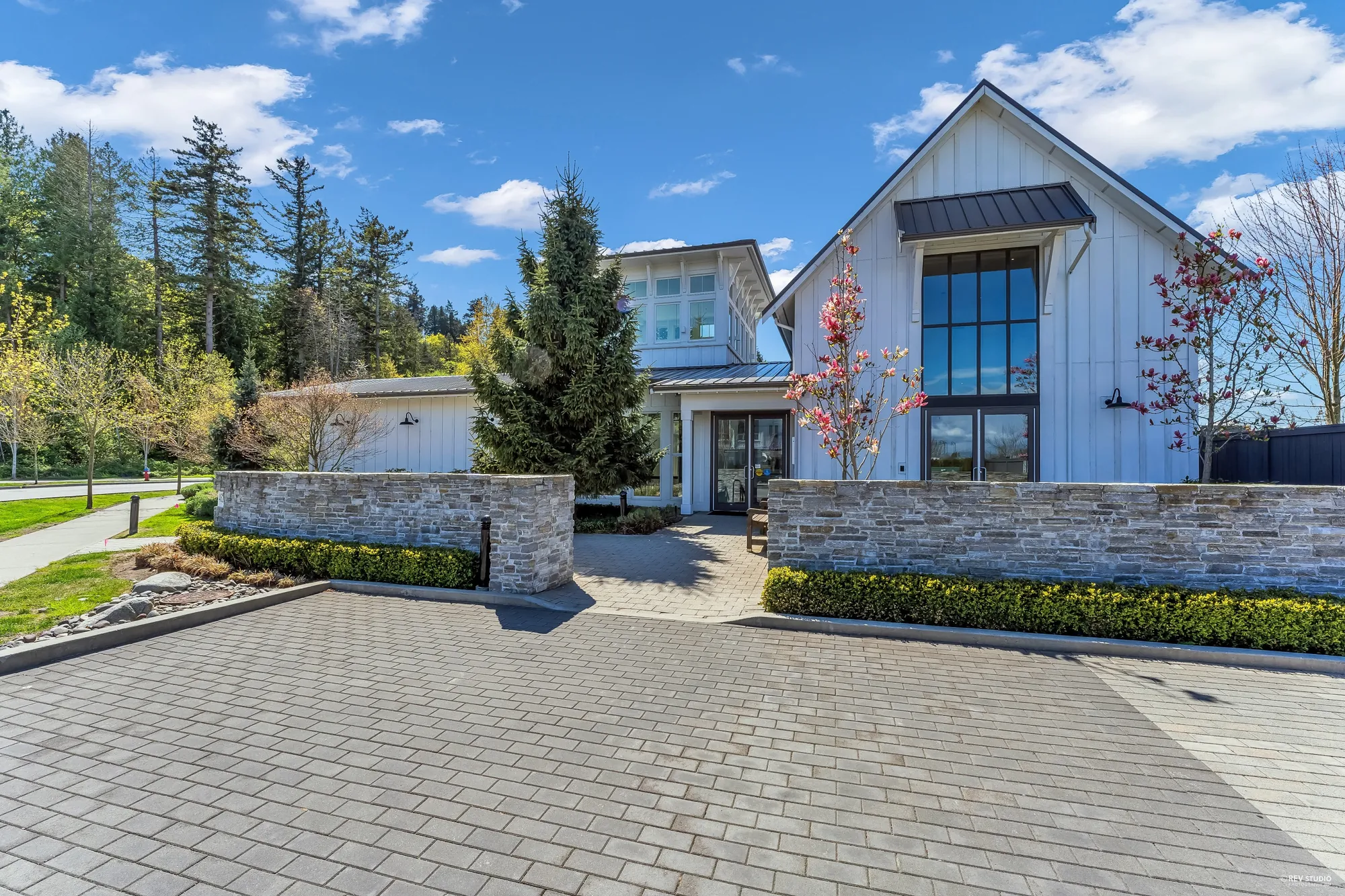 The clubhouse: white board-and-batten under steep gables, stone planters and a paved forecourt, trees behind