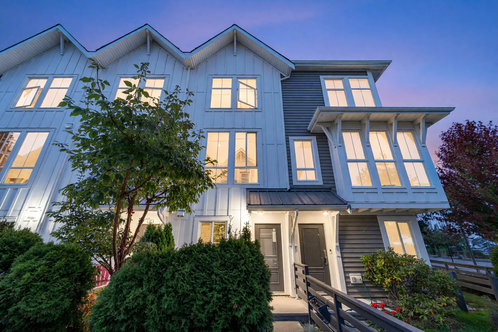 The front of 41's building at Seaside South at dusk: white board-and-batten siding under three gables, a grey-sided bay with tall windows, the windows lit against a violet sky