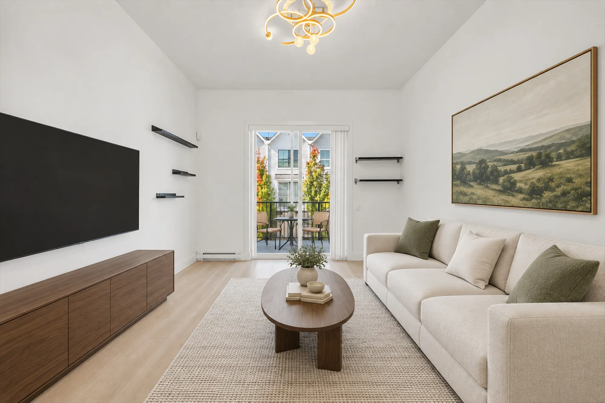 The living room virtually staged, toward the sliding door to the balcony: a cream sofa, an oval coffee table on a jute rug, a long walnut console under the TV, a landscape painting, black floating shelves, a gold ceiling fixture
