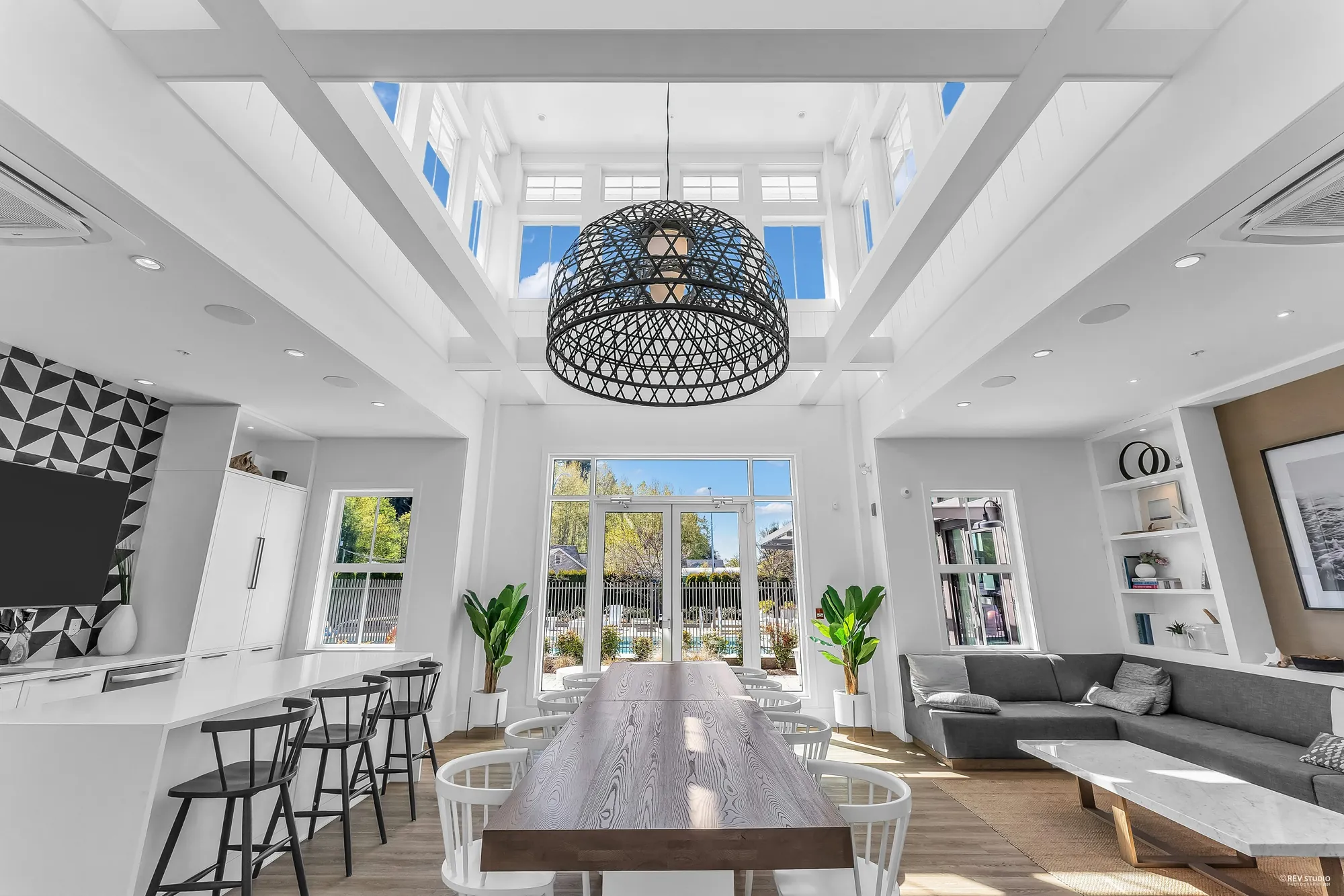 Inside the clubhouse: a double-height room with a long table under a lantern pendant, a sectional sofa, a counter with stools