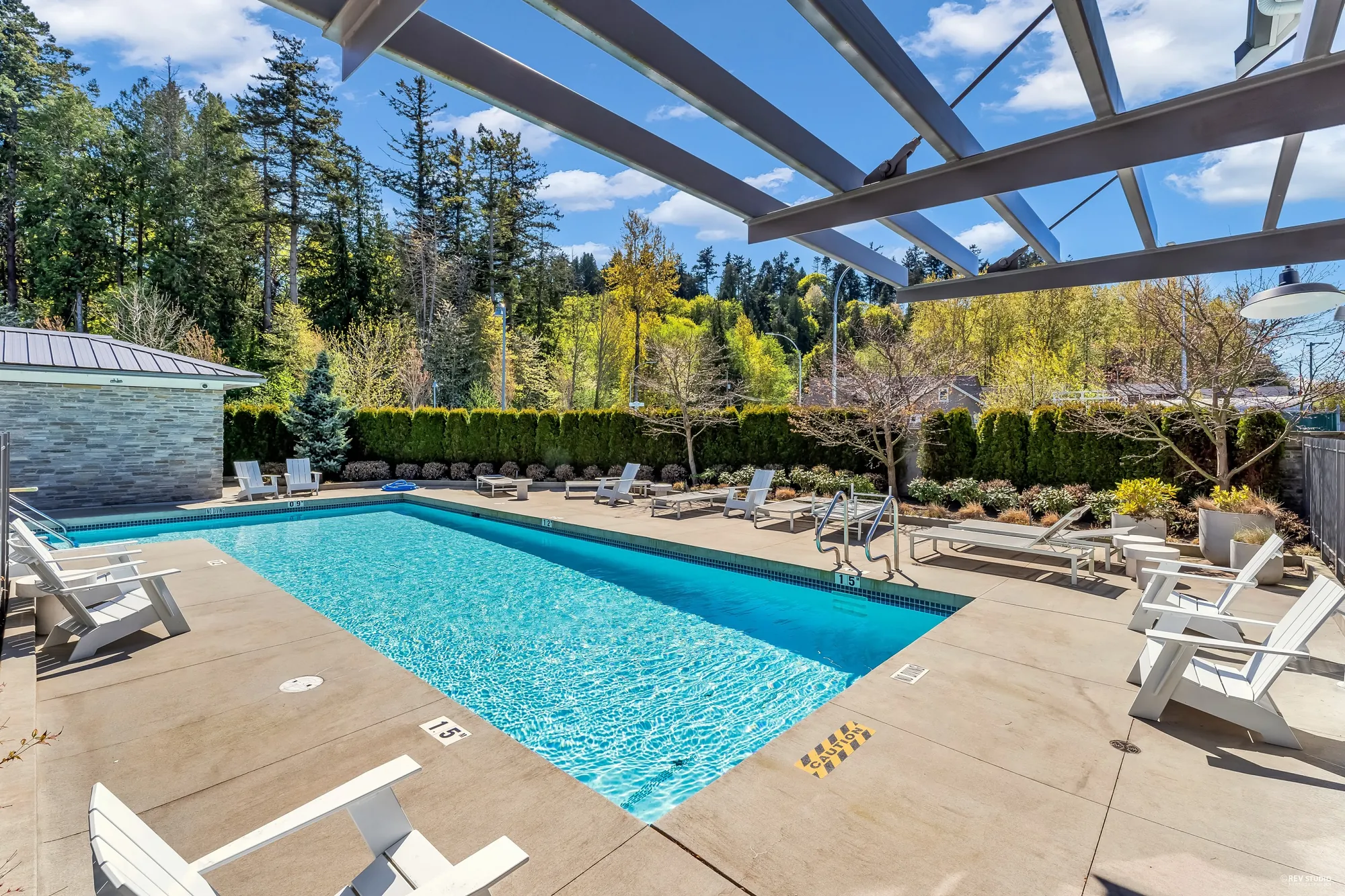 The outdoor pool beside a pergola, loungers along the deck, hedges and trees around
