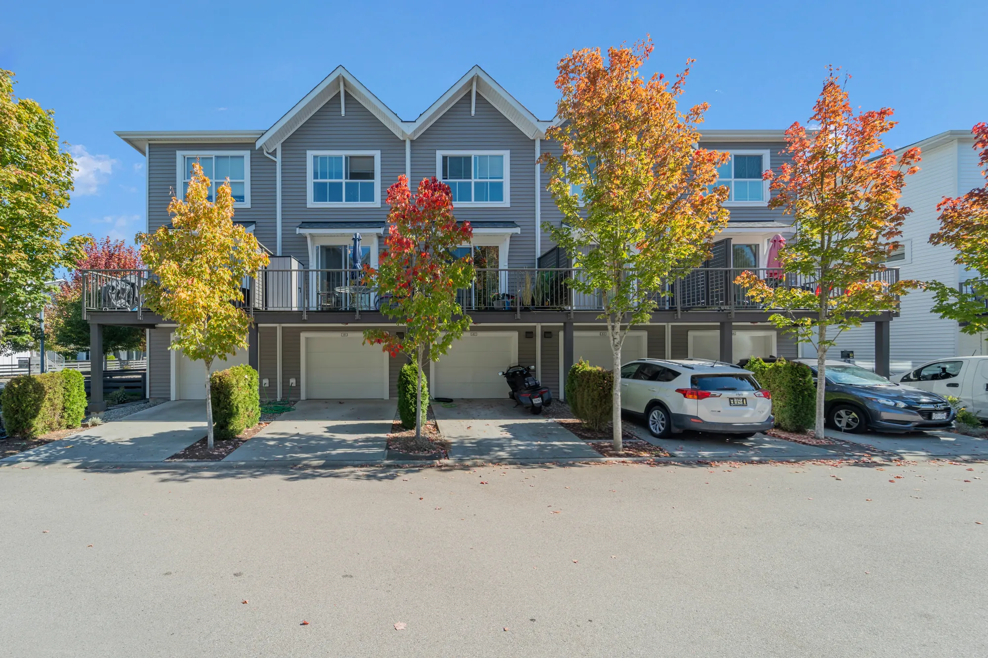The back of the row from the lane: garages below, balconies with railings above, maples in autumn colour, cars on the aprons